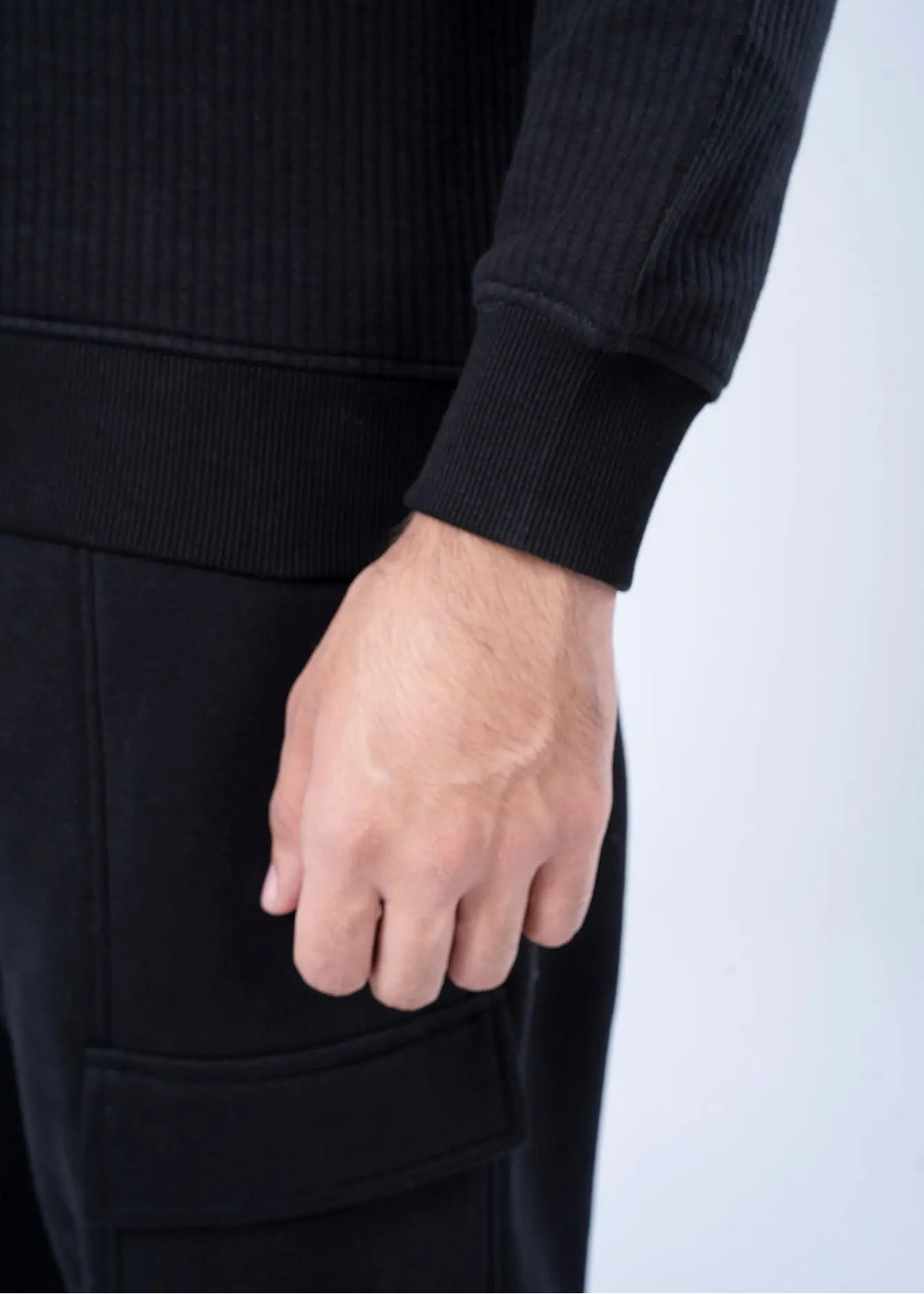 Black waffle-knit sweatshirt cuff and hand, with front pocket detail