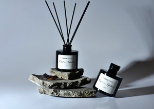 Black reed diffuser bottle with dark reeds on stacked stone-style discs, plus small bottle