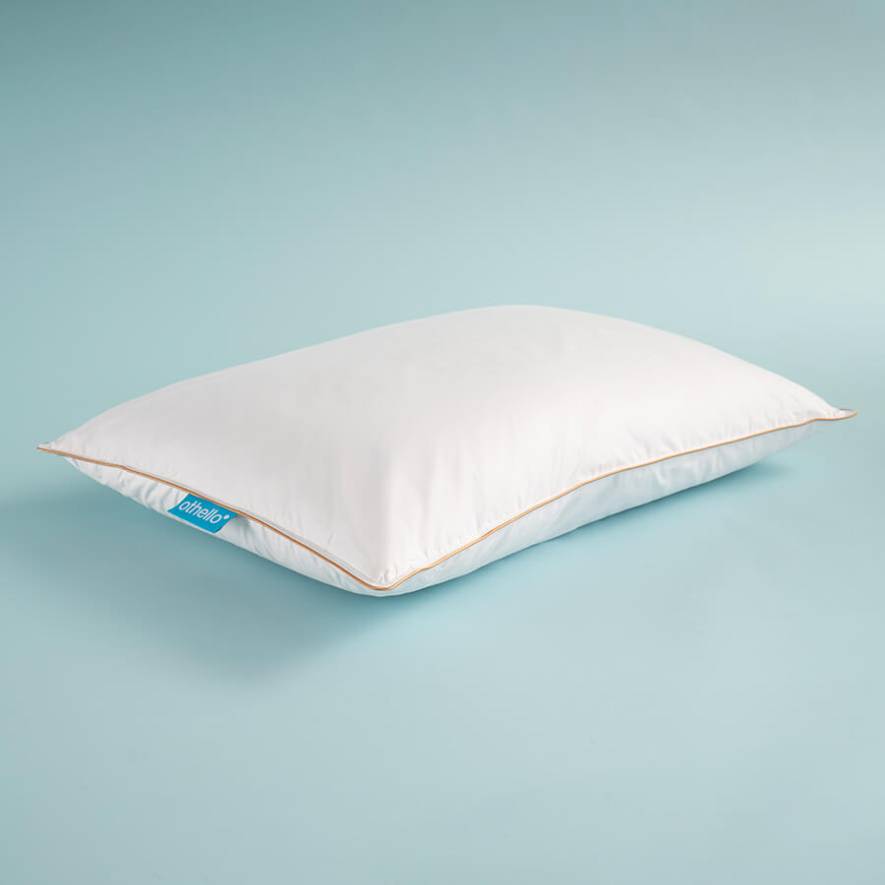 White down-filled pillow, angled view, with orange piping and blue brand tag.